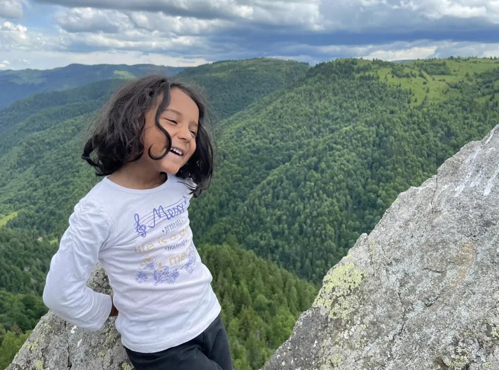 A smiling girl leaning on a rock above a forested mountain valley